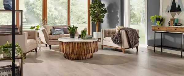 Sala de Estar Luminosa con Piso Vinílico SPC Sala de estar moderna y luminosa con grandes ventanales, sofá y sillones claros, mesa de centro de madera y un elegante piso vinílico SPC de tono gris claro.