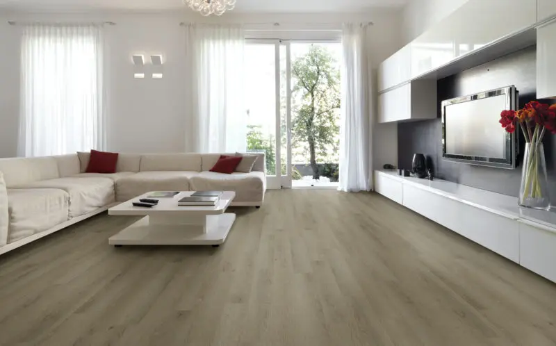 Amplia sala de estar moderna con sofá blanco, mesa de centro y mueble de TV, destacando un elegante piso vinílico SPC de tono madera clara.