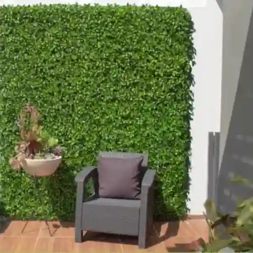 Terraza exterior de una residencia en Haras del Bosque con un gran muro cubierto de follaje artificial verde intenso, un sillón individual de exterior con cojín gris y una maceta colgante decorativa.