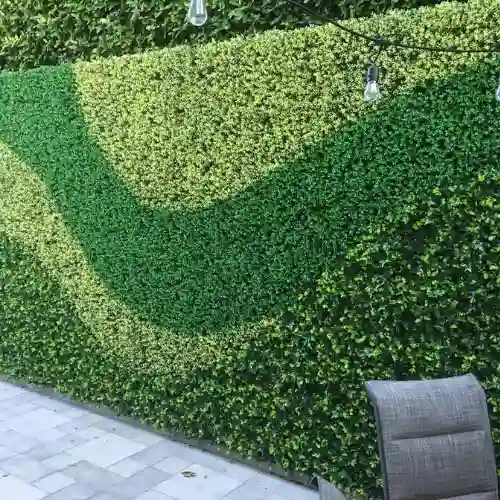 Muro exterior de un patio residencial en La Calera, Puebla, decorado con follaje artificial de diferentes tonos de verde en un patrón de olas, con luces de exterior colgando sobre el espacio.