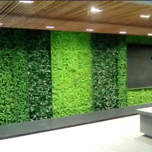Interior moderno de una oficina con una pared decorada con paneles de follaje artificial, combinando diferentes tonos de verde y texturas para un diseño elegante.