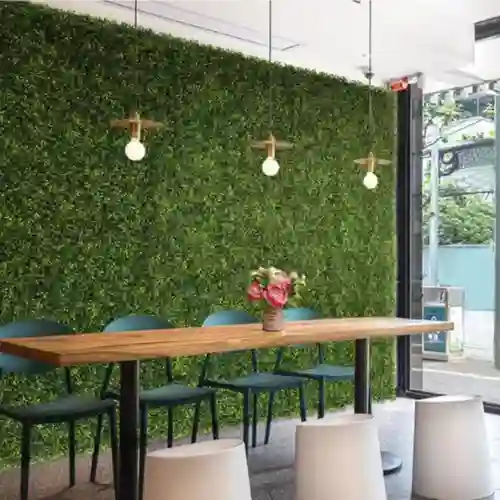 Muro de follaje artificial de diferentes tonalidades de verde en el patio de una residencia en la zona de El Cristo Residencial, con una mesa larga de madera y sillas de diseño.