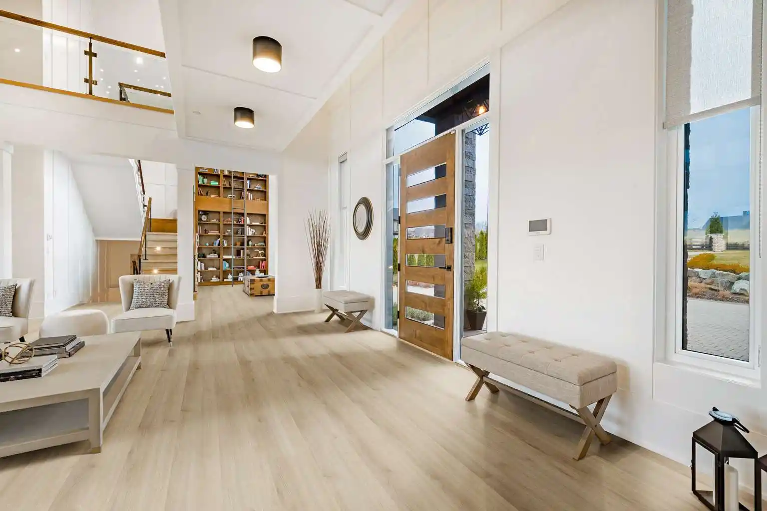 Piso vinílico de tablones amplios en tono madera clara instalado en una espaciosa entrada de casa moderna, con puerta de madera, paredes blancas y mobiliario minimalista, ideal para un diseño contemporáneo en Puebla.