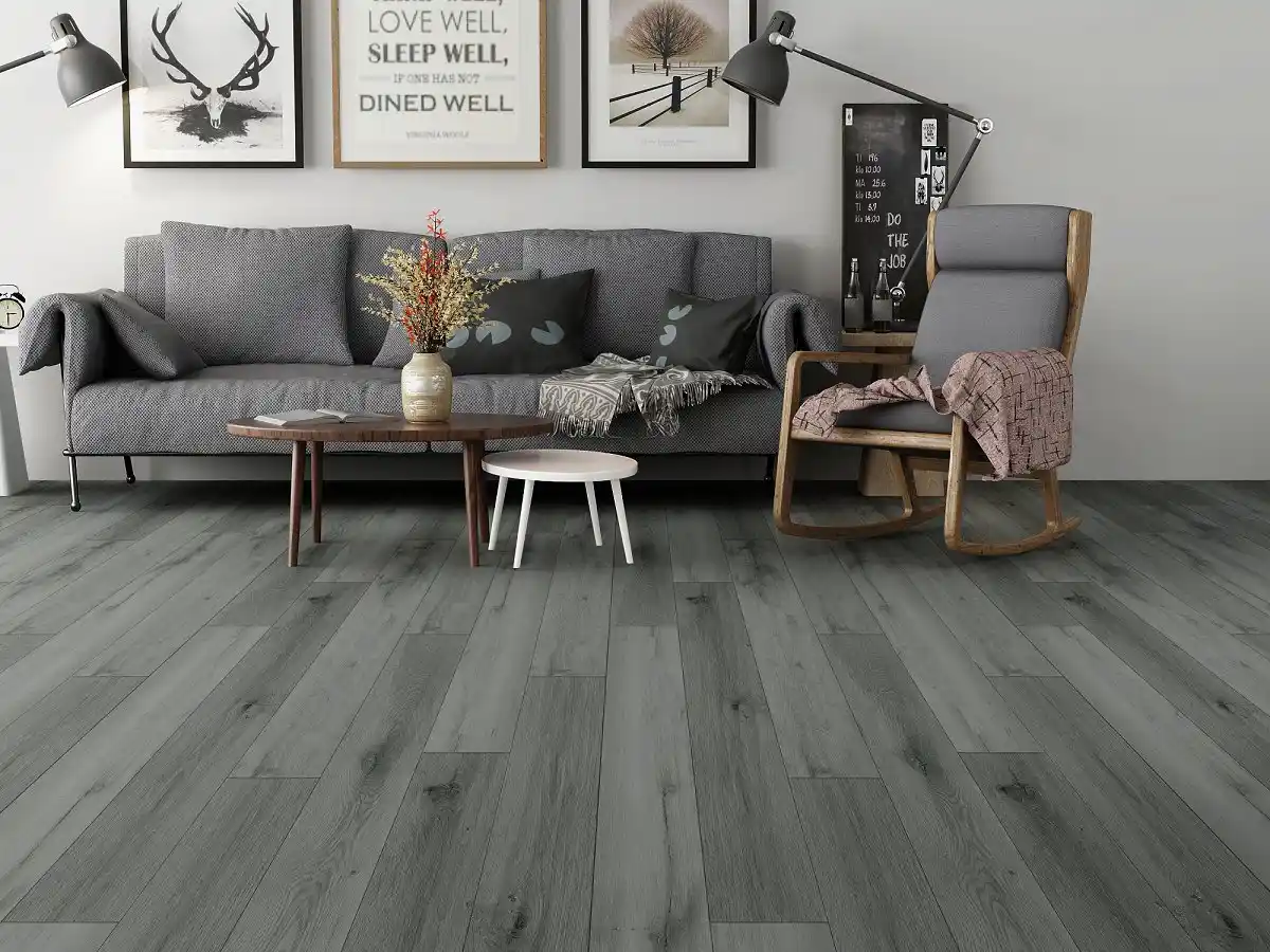 Piso vinílico de tablones en tono gris claro, instalado en una sala de estar moderna con sofá gris, silla mecedora de madera y cojines decorativos, ideal para un ambiente acogedor en Puebla.