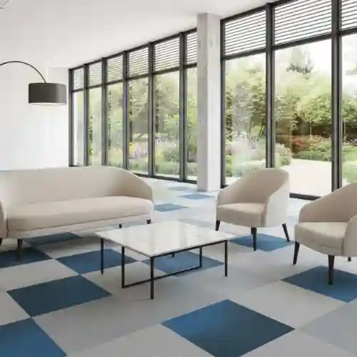 Sala de espera moderna con losetas de alfombra modular instaladas en un patrón de ajedrez azul y gris, una solución de diseño versátil de Grupo Orvi para oficinas en Puebla.