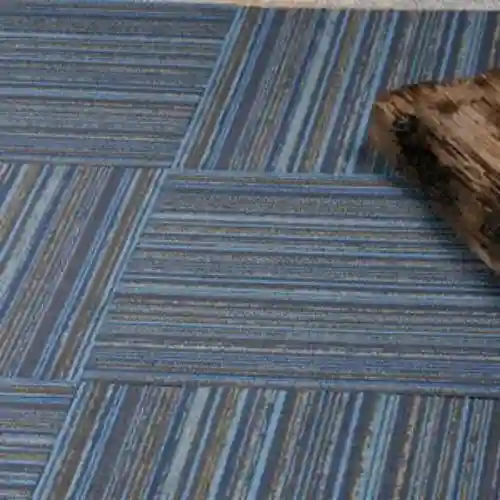 Detalle de un piso con losetas de alfombra modular instaladas en diferentes ángulos para crear un patrón geométrico moderno en tonos azules y grises, una solución de diseño de Grupo Orvi.