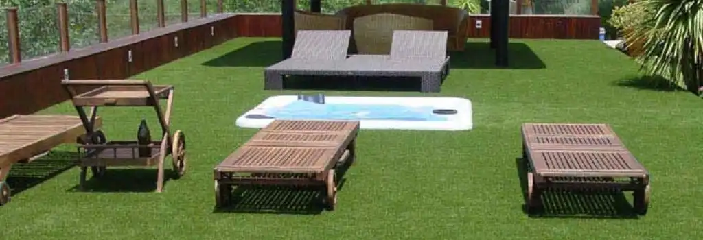 Terraza con pasto sintético residencial de alta calidad, con jacuzzi blanco y camastros de madera, demostrando una instalación premium para descanso y ocio en Puebla.